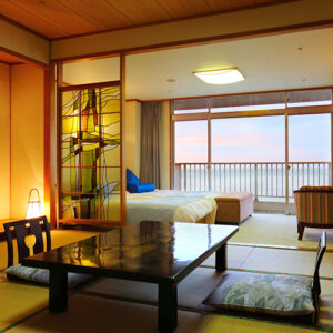 ベッド、畳テーブル、海に面した窓のある客室