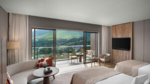 ベッド2台、くつろぎスペース、バルコニー越しの山の眺め