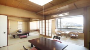 Habitación de tatami con mesas bajas, sillas y asientos junto a la ventana