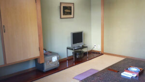 Habitación de tatami con cojines en el suelo, mesa baja y televisión