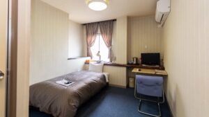 Single bed beside desk and window in guest room