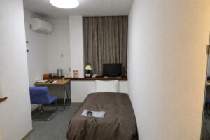 Single bed in narrow guest room with desk and TV