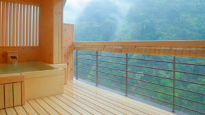 Baño al aire libre en un balcón de madera con vistas a montañas boscosas