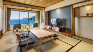 Habitación de tatami con mesa baja, sillas y vista al océano