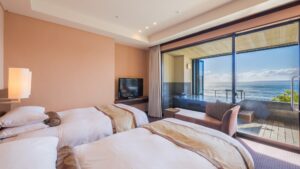 Camas individuales junto a un balcón con vista al mar y zona de estar