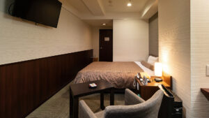 Habitación con cama, silla, mesa y TV montada en la pared