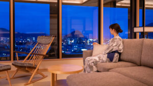Mujer sentada en un sofá junto a grandes ventanales por la noche