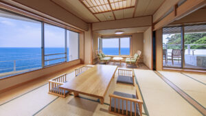 Chambre en tatami avec table basse, chaises et fenêtres donnant sur l’océan