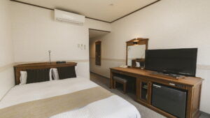 Bed facing desk, television, and mini fridge
