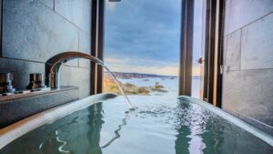 Bain privé avec vue sur l’océan à travers la fenêtre ouverte