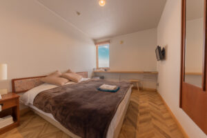 Schlafzimmer mit Doppelbett, Schreibtisch und wandmontiertem Fernseher