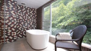 Freestanding bath beside window with chair and forest view