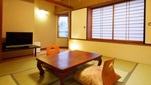 Tatami-Zimmer mit niedrigem Tisch, Bodensesseln und Fernseher