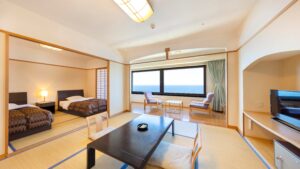 Tatami-Gästezimmer mit niedrigem Tisch, Betten und Fenster mit Meerblick
