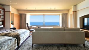 Zwei Einzelbetten und ein Sofa vor einem großen Fenster mit Meerblick