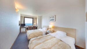 Zweibettzimmer mit Betten zum Fenster und Schreibtisch ausgerichtet