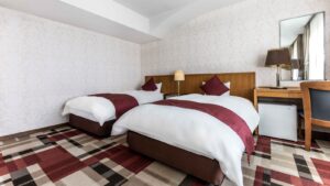 Two beds in a guest room with desk and mirror
