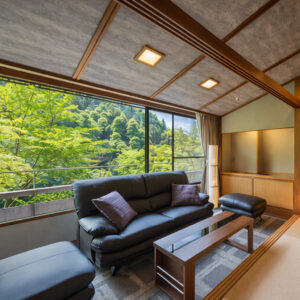 Sitzbereich mit Sofa neben großem Fenster mit Waldblick