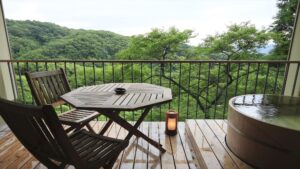 木々を望むバルコニーのテーブルと椅子のそばにある木風呂