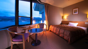 Cama junto a la ventana con sillas y vista al océano