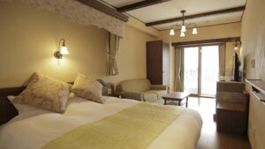 ツインベッド、アームチェア、テーブル、バルコニードアのある寝室