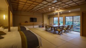 Tatami-Zimmer mit Betten, Esstisch und Sitzbereich am Fenster