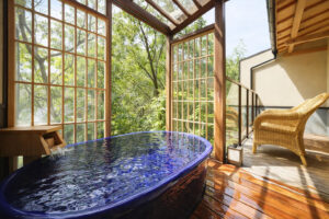 Blaue Badewanne neben großen Fenstern und Korbstuhl