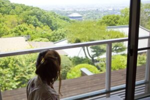 Frau am Fenster mit Blick auf Bäume und die Stadt in der Ferne