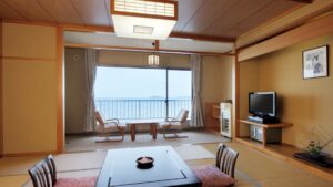 Habitación de tatami con mesa baja, sillas y vista al mar