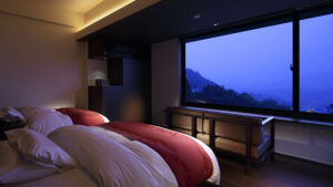 Twin beds beside a large window with mountain view