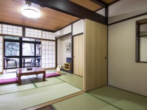 Tatamizimmer mit niedrigem Tisch, Bodenkissen und Stühlen am Fenster