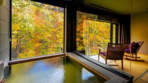 Privates Bad am Fenster mit Blick auf herbstliche Bäume und Stühle