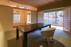 Tatami-Zimmer mit niedrigem Tisch, Stuhl und Fenstern zum Garten