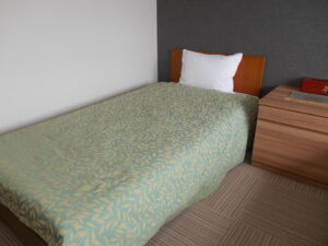 木製ナイトスタンドの横にある柄付きベッドカバーのシングルベッド