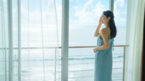 바다 전망이 보이는 발코니 창가에 서 있는 여성