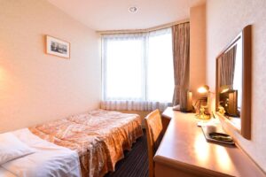 Single bed beside desk and window in guest room