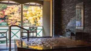 Baño interior de piedra junto a ventanas con árboles otoñales afuera
