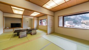 Chambre en tatami avec table basse, chaises au sol et vue par la fenêtre