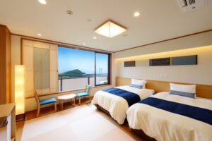 Twin beds beside window with chairs and ocean view