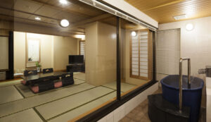 Bain privé à côté d’une chambre d’hôtes en tatami, vu à travers une fenêtre en verre