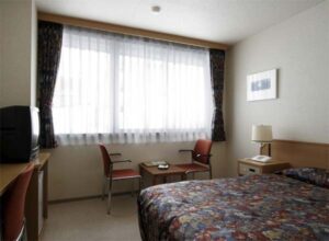 Bett und Stühle neben einem großen Fenster mit Vorhängen