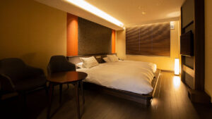 Zwei Betten neben Stühlen in einem sanft beleuchteten Zimmer