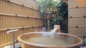 Round wooden open-air bath beside bamboo fencing